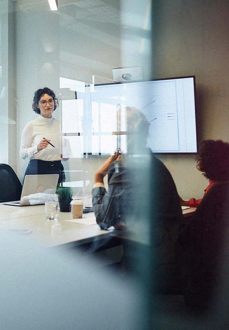 Strategie-Workshop und Digitalmarketing-Beratung: Eine Beraterin präsentiert Analyse-Diagramme auf einem Bildschirm vor einem Team im Konferenzraum.