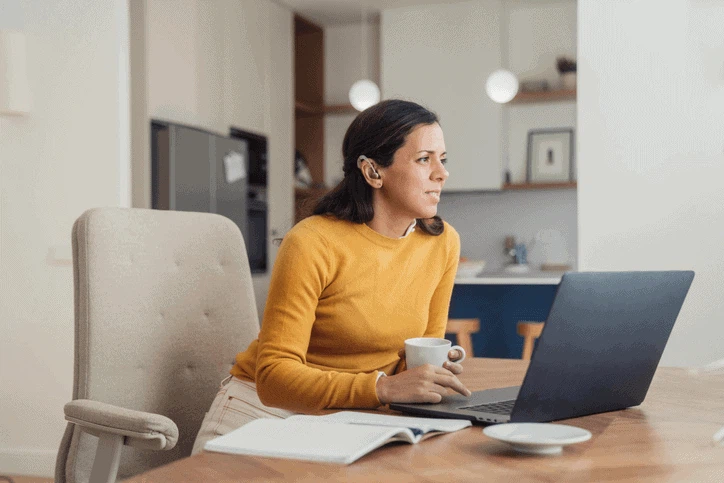 Barrierefreiheit auf Websites nach dem BaFG: Eine Frau mit Hörgerät arbeitet konzentriert an einem Laptop.