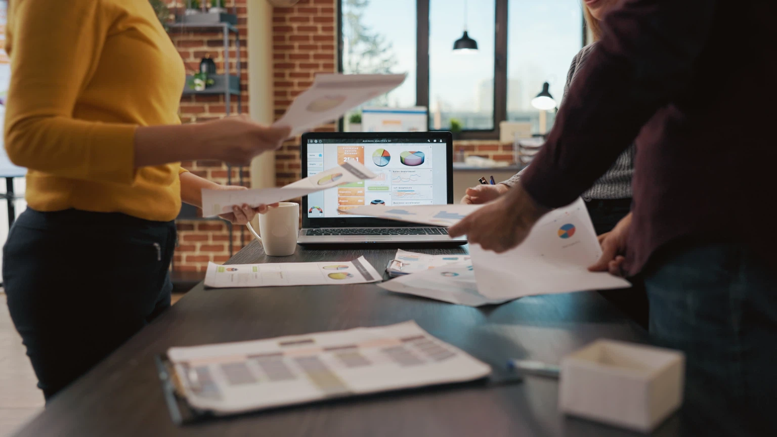 Team bei der Datenanalyse und Vertriebsplanung: Mehrere Personen besprechen Diagramme und Berichte an einem Tisch mit Laptop.