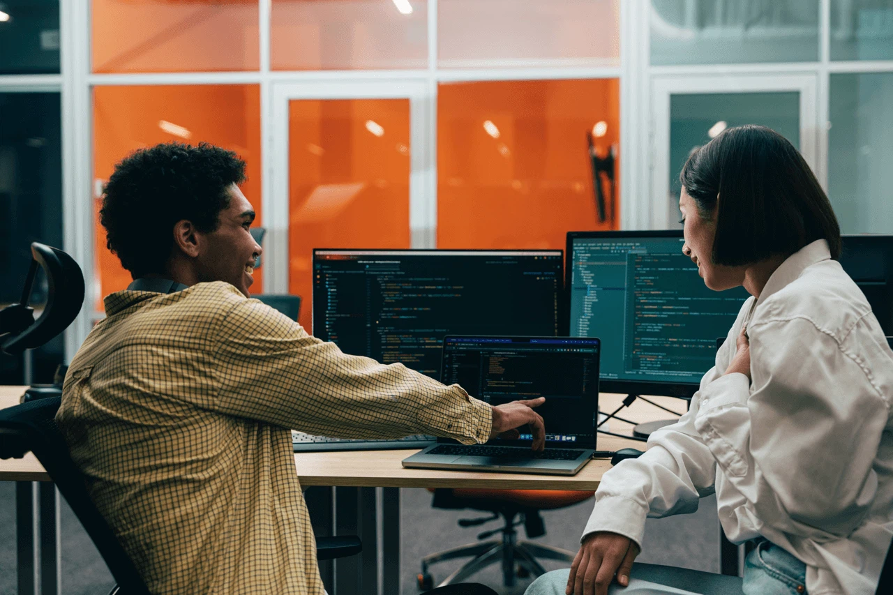 WordPress vs. TYPO3 CMS-Vergleich: Zwei Webentwickler der MMCAgentur analysieren Programmcode an Monitoren für eine optimale Website-Architektur.