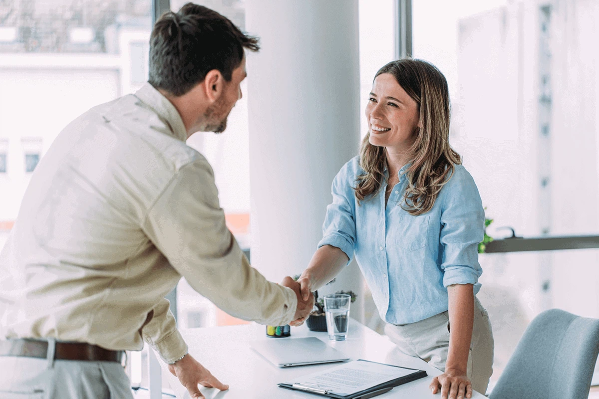 Erfolgreiches Social Recruiting mit der MMCAgentur: Eine HR-Managerin besiegelt die Einstellung eines neuen Mitarbeiters mit einem Händedruck im Büro.