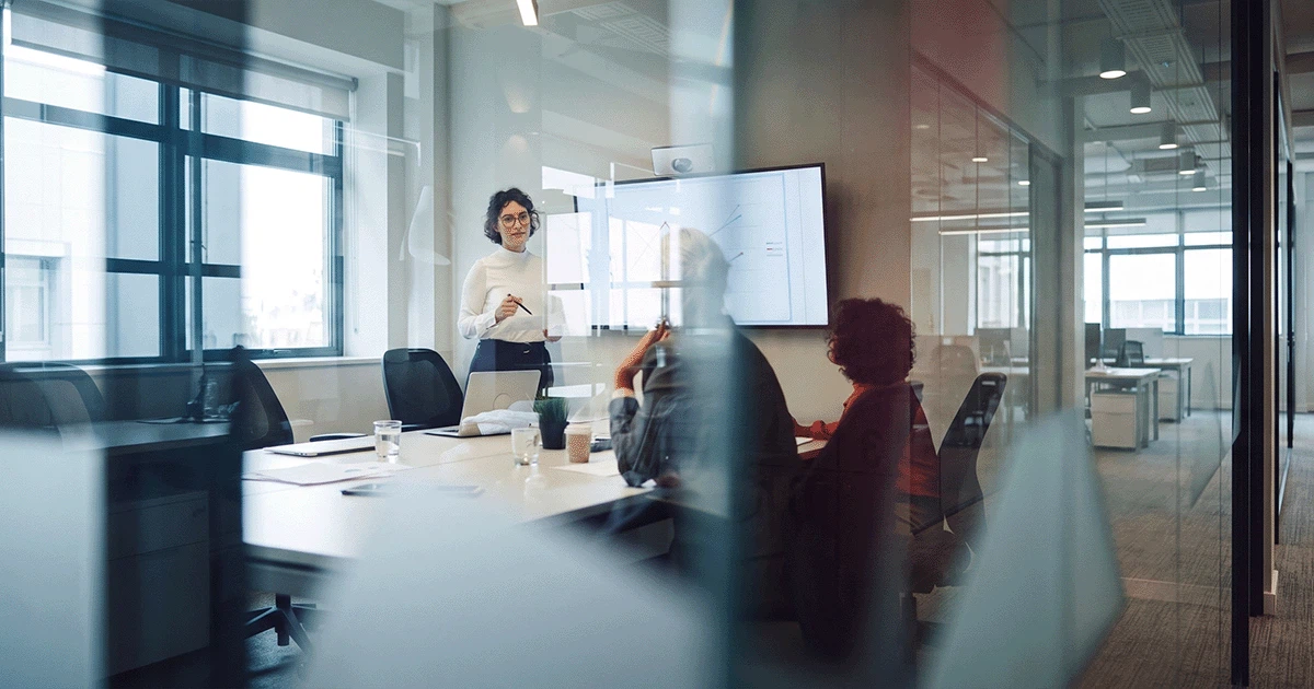 Strategie-Workshop und Digitalmarketing-Beratung: Eine Beraterin präsentiert Analyse-Diagramme auf einem Bildschirm vor einem Team im Konferenzraum.