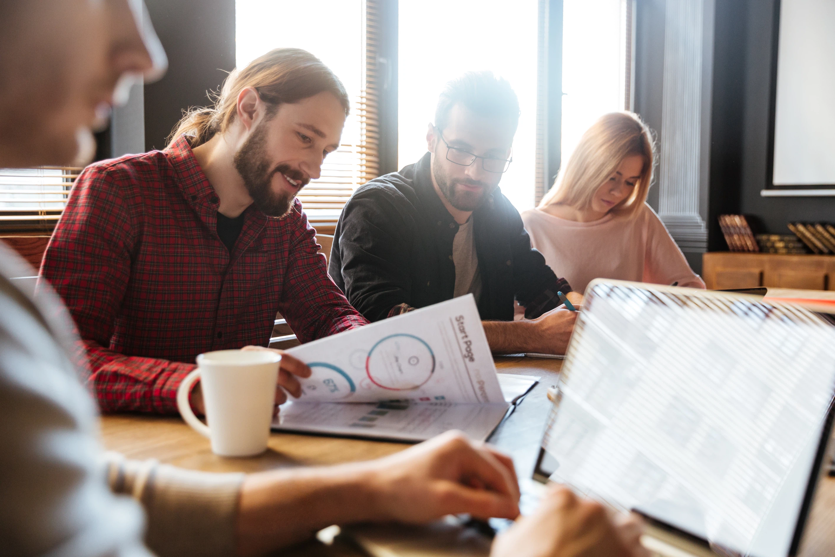 Strategie-Workshop und Zusammenarbeit im Team: Mehrere Personen arbeiten gemeinsam mit Unterlagen und Laptop an einem Besprechungstisch.